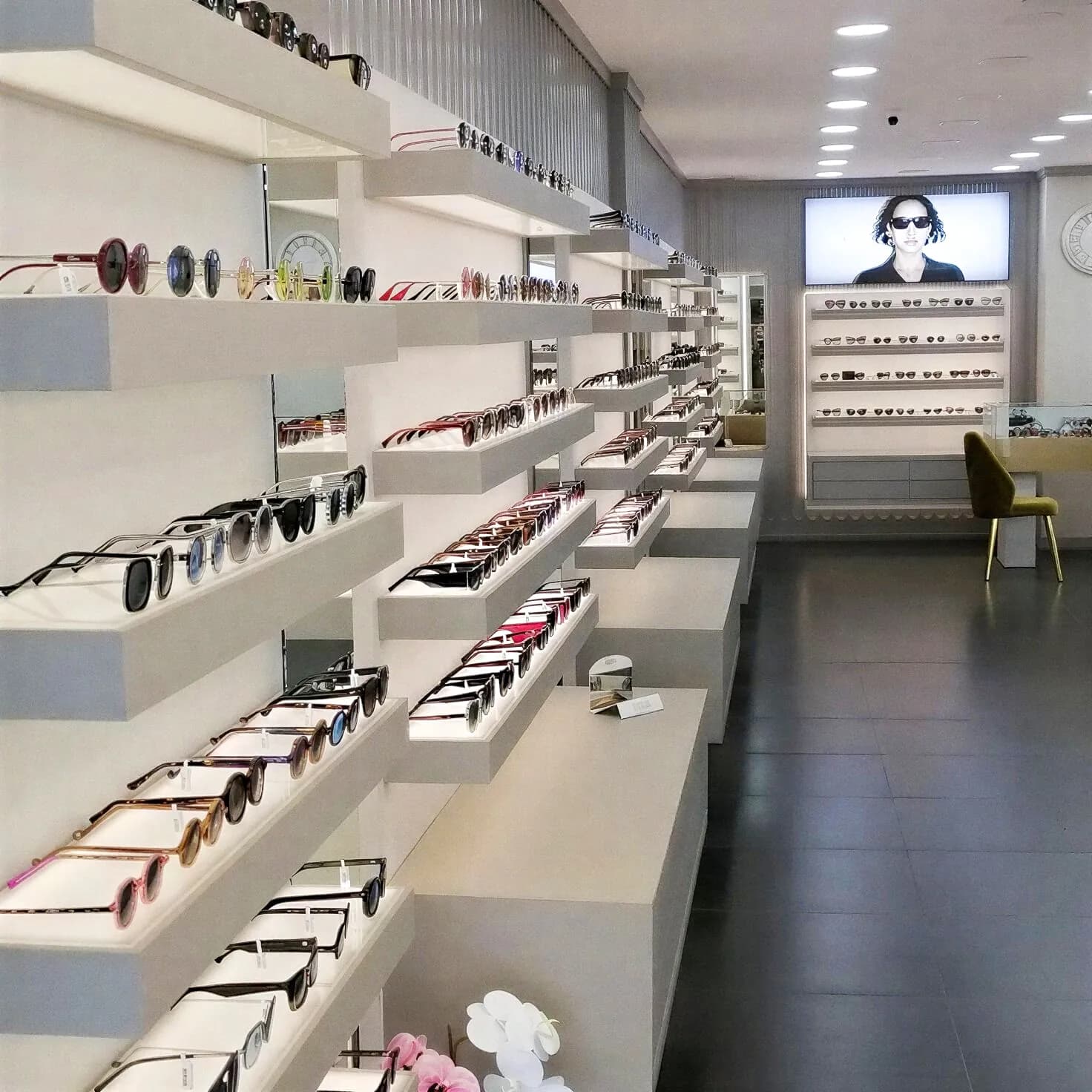 Optical store with white stepped display shelves for sunglasses and modern minimalist design