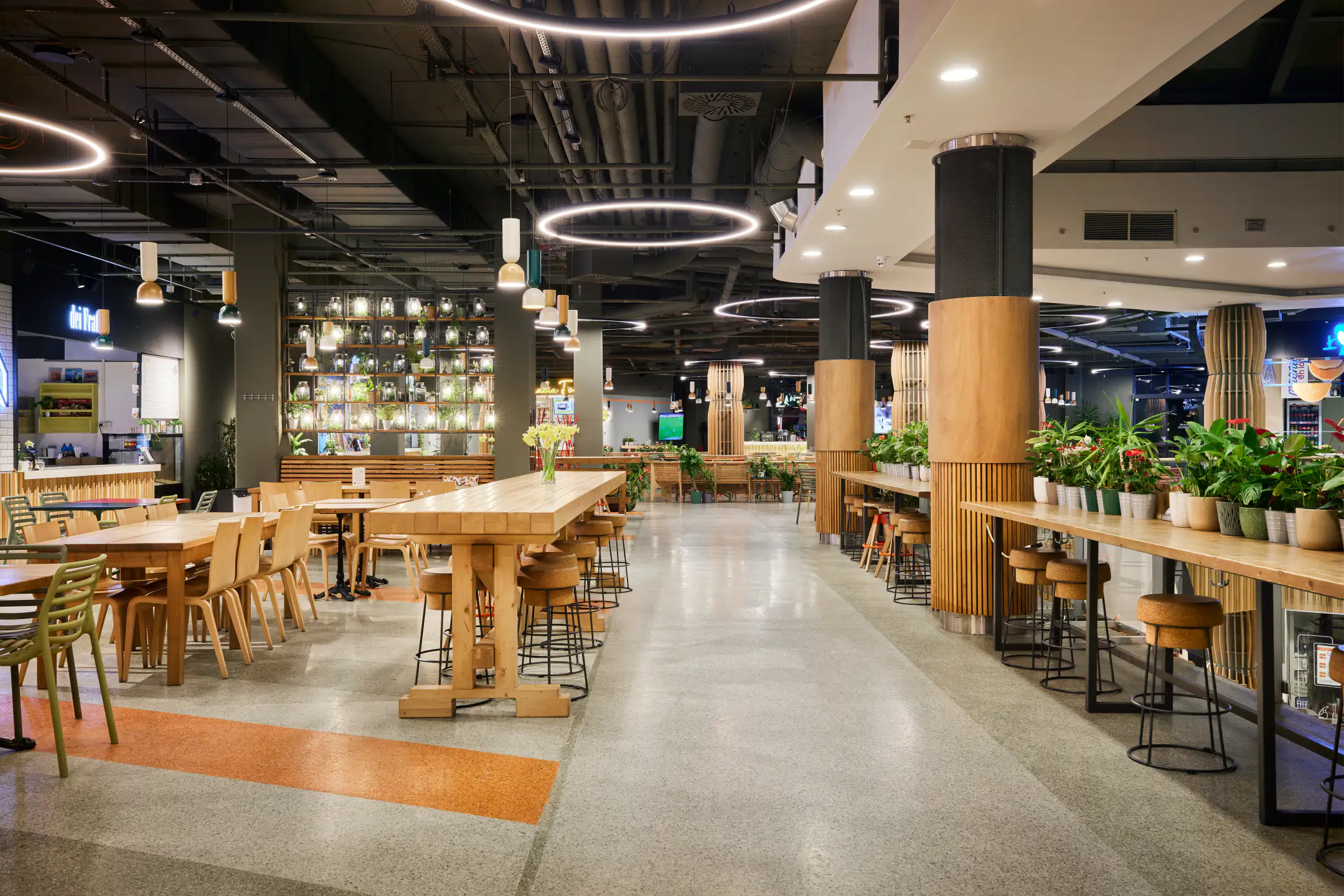 Beverage bar with backlit bottle wall, tall wooden tables and suspended ring lights